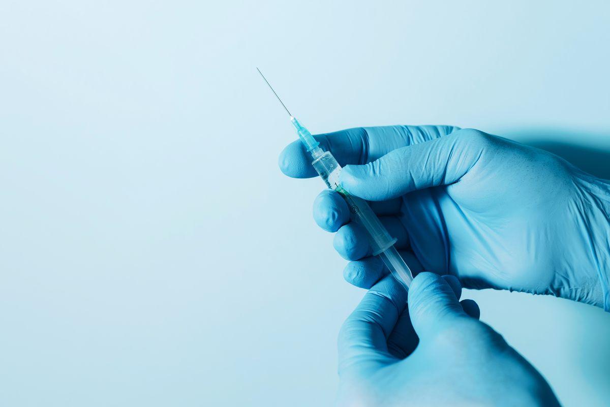 syringe-held-in-gloved-hands-against-blue-backgrou-2026-03-10-01-00-28-utc